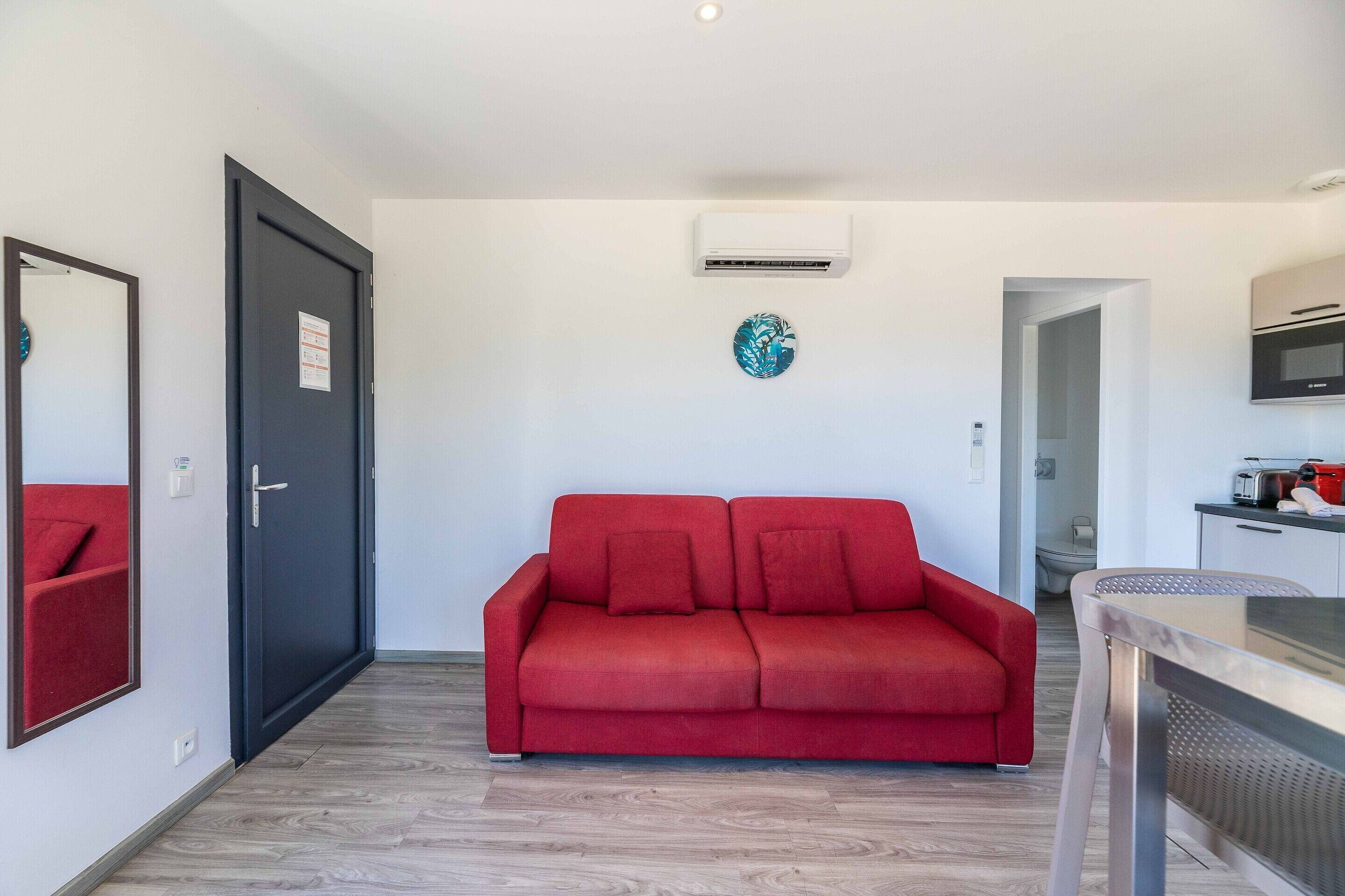 Ein modernes Zimmer mit einem roten Sofa, einem Esstisch, einer Küchenzeile und einer Tür.