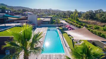 A swimming pool with a wooden deck, surrounded by palm trees and shaded areas.