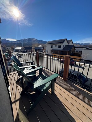 A balcony with green chairs, a view of a parking lot, and buildings with a mountain backdrop. - Cozy mountain townhome in beautiful Salida (Salida)