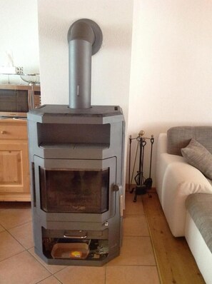 A wood-burning stove in a living room with a sofa and a wooden cabinet. - Chalet Bergblick in Sachrang Bavaria for 4 Guests - Experience Pure Nature! (Aschau im Chiemgau)