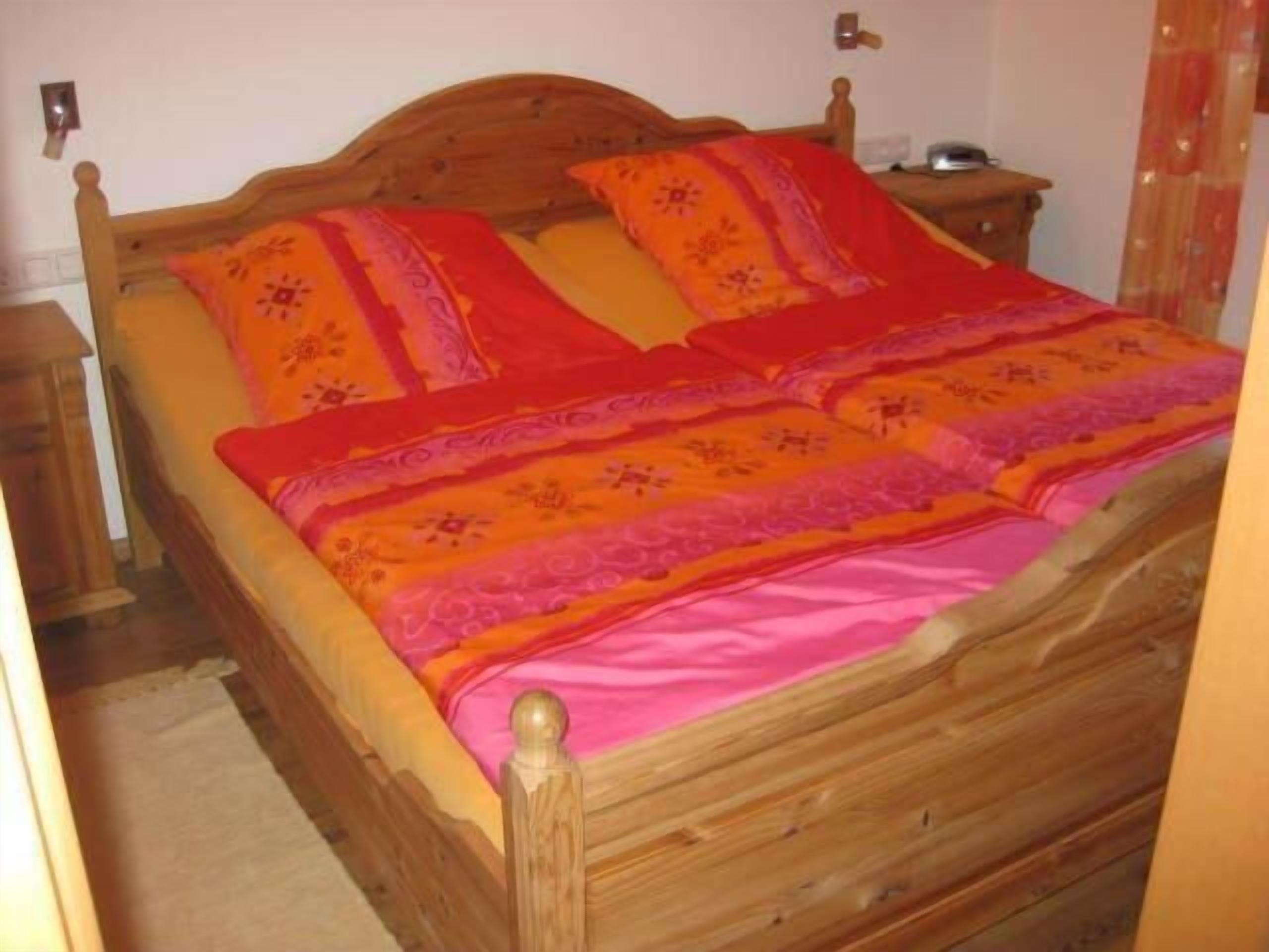 Una cama de madera con cabecera, dos almohadas y una colcha.