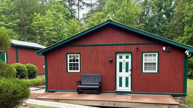 A red wooden cabin with a green door, a bench outside, and a grassy yard. - 2-bedroom cabin in serene Cleveland perfect for a relaxing getaway (Cleveland)