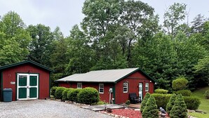 A red building with a gravel driveway, a small shed, and a well-maintained garden with red mulch and green shrubs. - 2-bedroom cabin in serene Cleveland perfect for a relaxing getaway (Cleveland)