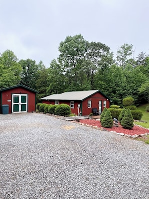 A red building with a gravel driveway, a small shed, and a well-maintained garden with red mulch and green shrubs.