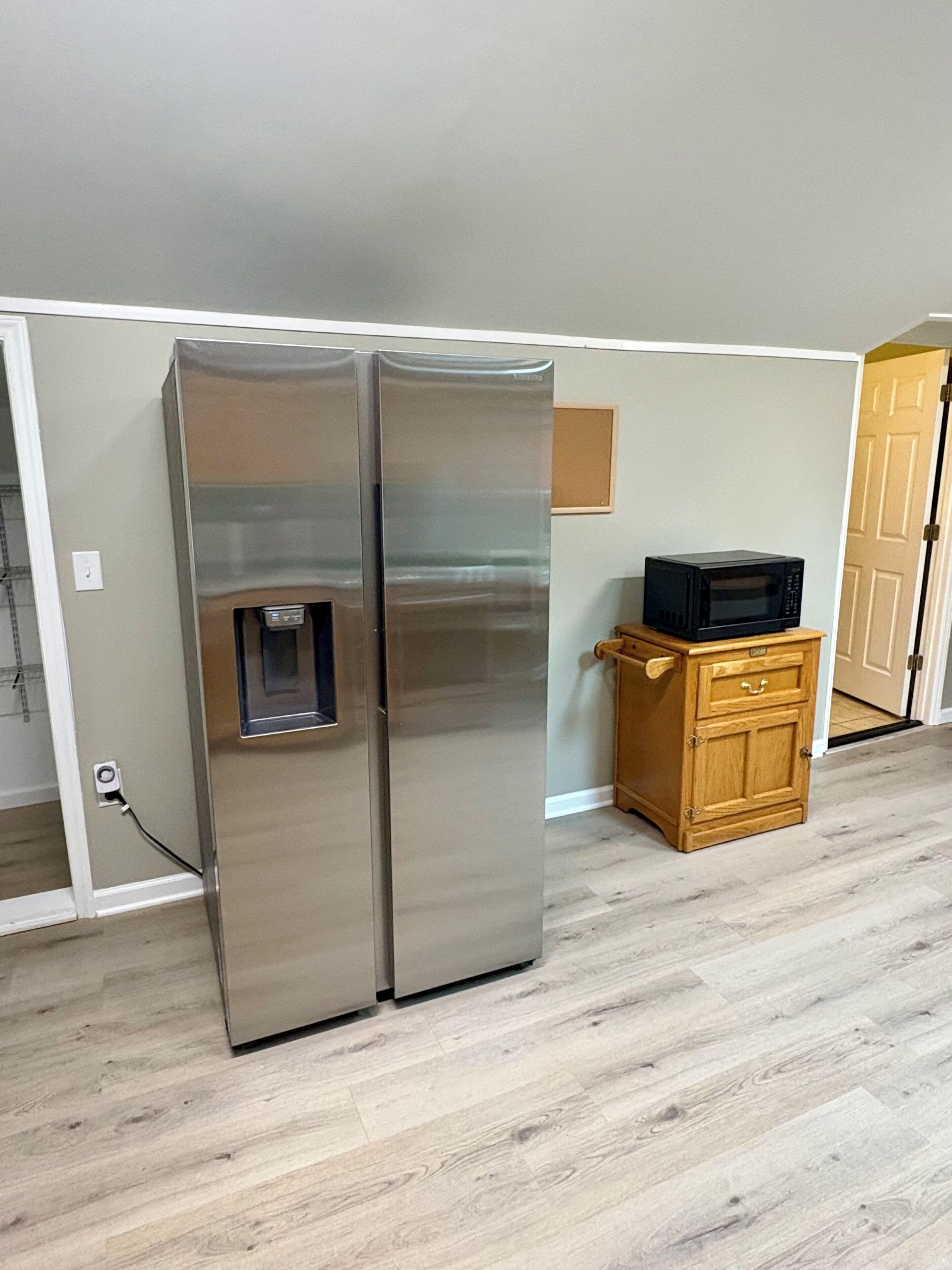 Una cocina con un refrigerador de acero inoxidable, un mueble de madera y un microondas sobre una encimera.