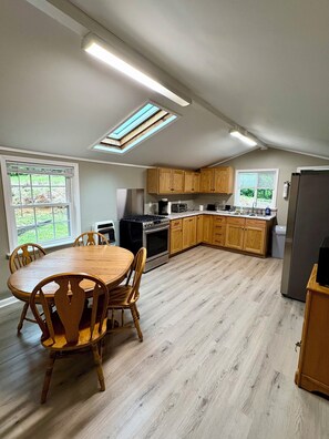 A kitchen with wooden cabinets, a dining table with chairs, a refrigerator, and a skylight.