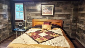 A bedroom with a wooden headboard, a quilted bedspread, a bedside table with a lamp, and a framed picture on the wall. - 2-bedroom cabin in serene Cleveland perfect for a relaxing getaway (Cleveland)