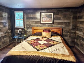 A bedroom with a wooden headboard, a quilted bedspread, a bedside table with a lamp, and a framed picture on the wall.