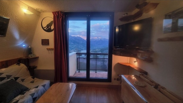 A room with a bed, a small table, a TV, and a balcony with a mountain view. - Panoramic view and mountain cocoon Pra-Loup 1500 (Uvernet-Fours)