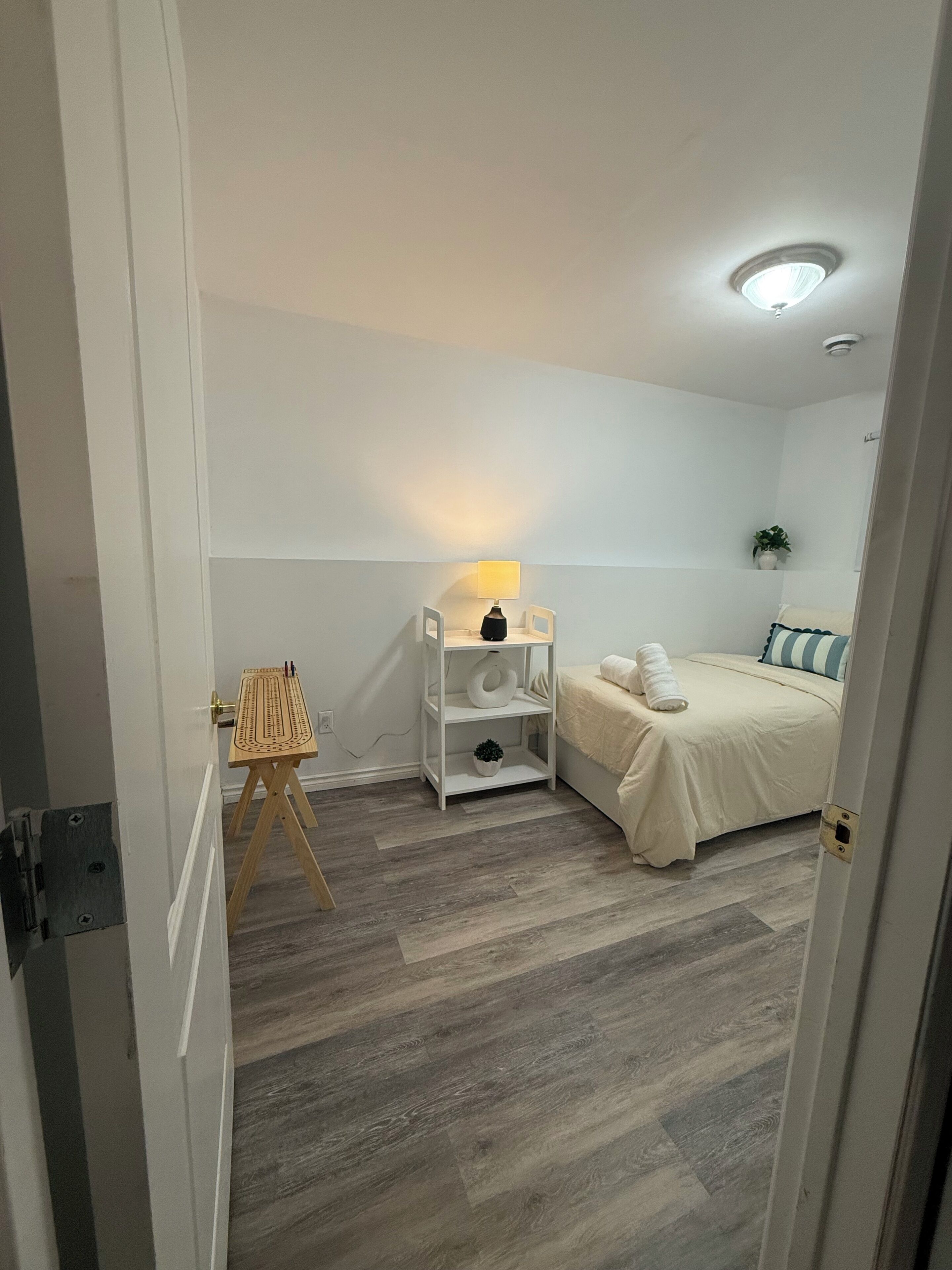 Un dormitorio con cama, mesitas de noche, lámpara, una pequeña mesa con una planta y suelo de madera.