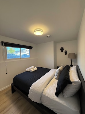 Une chambre à coucher avec un lit, une fenêtre, une lampe fixée au mur et un luminaire au plafond.