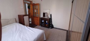A bedroom with a bed, a dresser, a mirror, a guitar, and a cabinet.