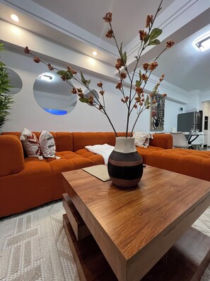 Uma sala de estar moderna com mesa de centro de madeira, sofá laranja e um vaso com galhos.
