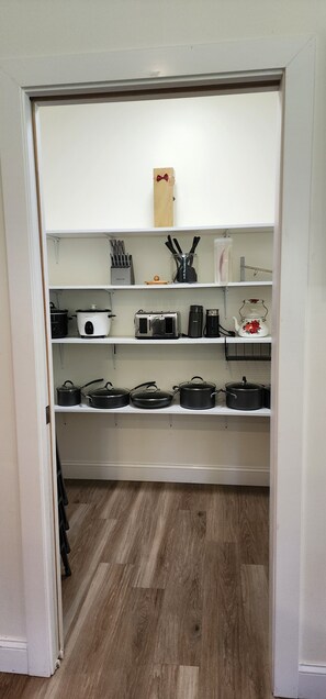 Una cocina con estantes blancos, una olla de cocción lenta, un tostador, un hervidor y una cafetera.