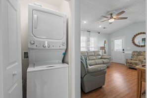 A laundry room with a front-loading washer and dryer, a ceiling fan, and a living room with a sofa and a coffee table. - Seas The Day, Waterpark, Close to Beach & Porch (Myrtle Beach)