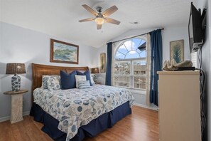 A bedroom with a bed, a ceiling fan, a window with curtains, a wall-mounted TV, and a decorative item on a cabinet. - Seas The Day, Waterpark, Close to Beach & Porch (Myrtle Beach)