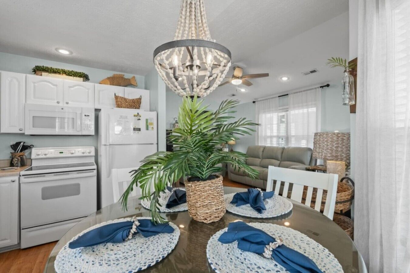 A modern kitchen with white appliances, a dining table set for four, and a large potted plant.