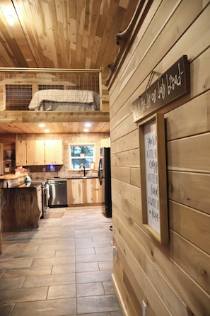 Un interior de madera con una zona de cocina, que incluye armarios, un refrigerador y un cartel en la pared.