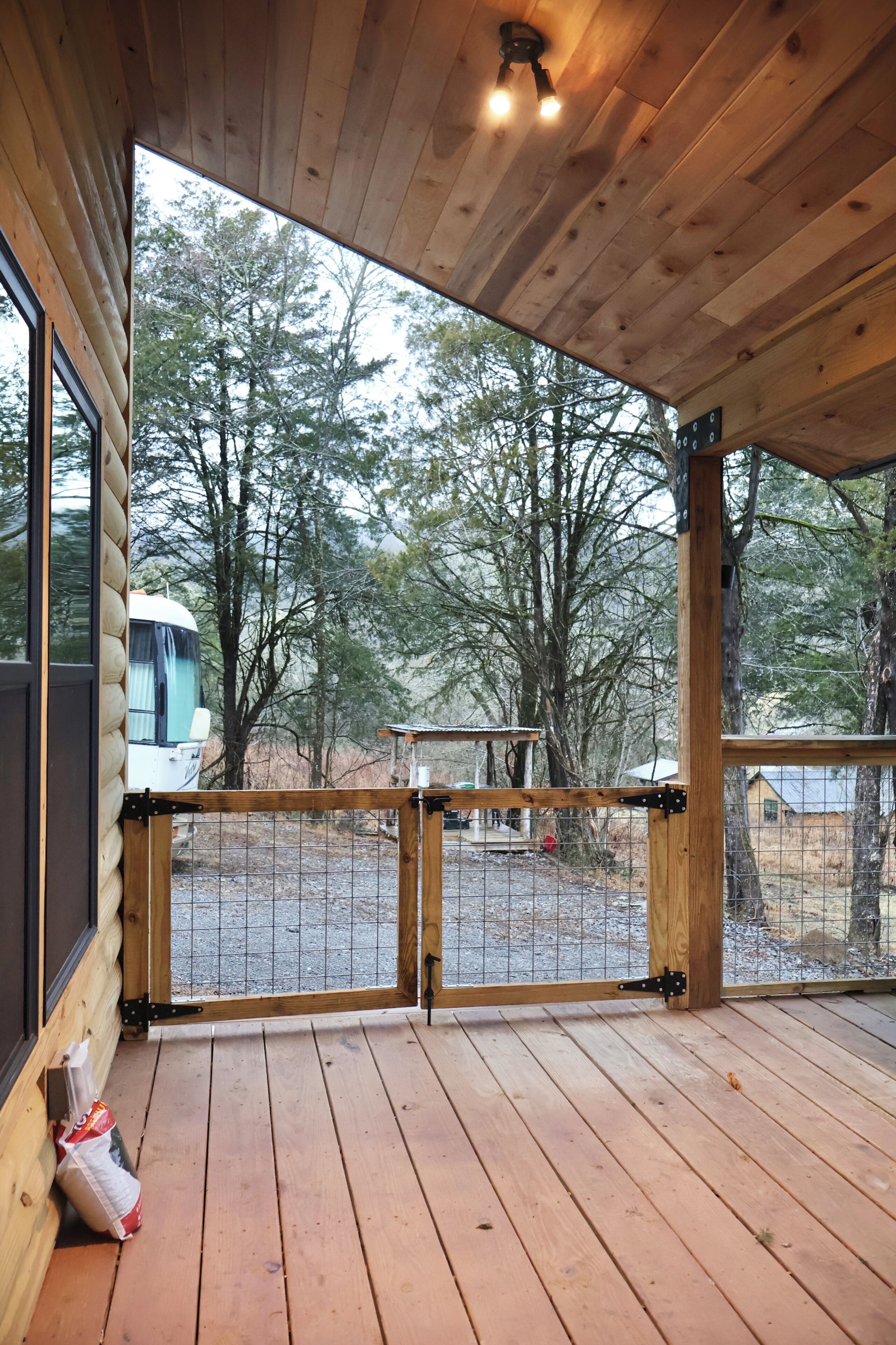 En træterrasse med udsigt over et skovområde og en autocamper.
