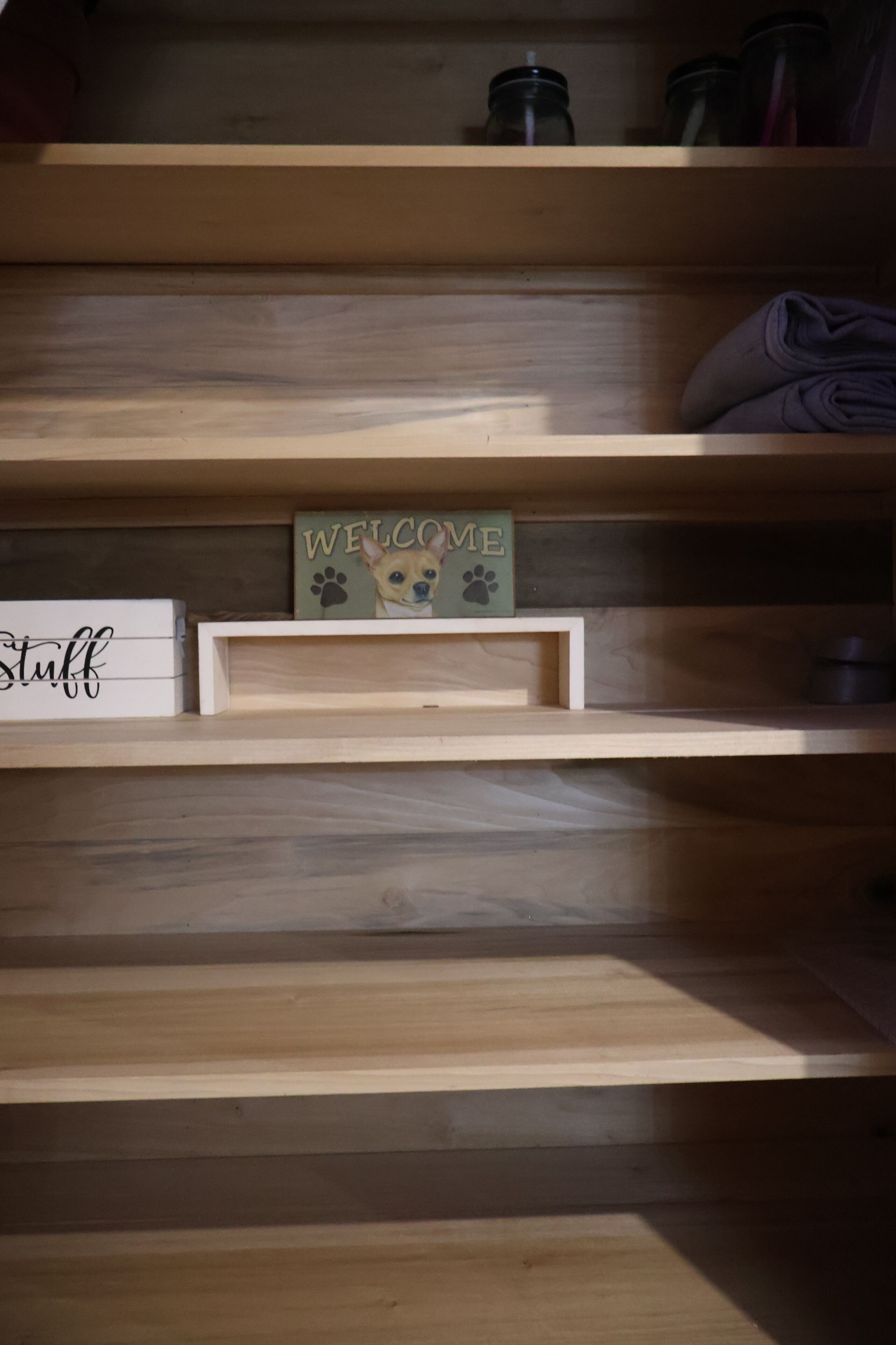 A wooden shelf with a 'Welcome' sign, a 'Stuff' sign, and a small framed picture.