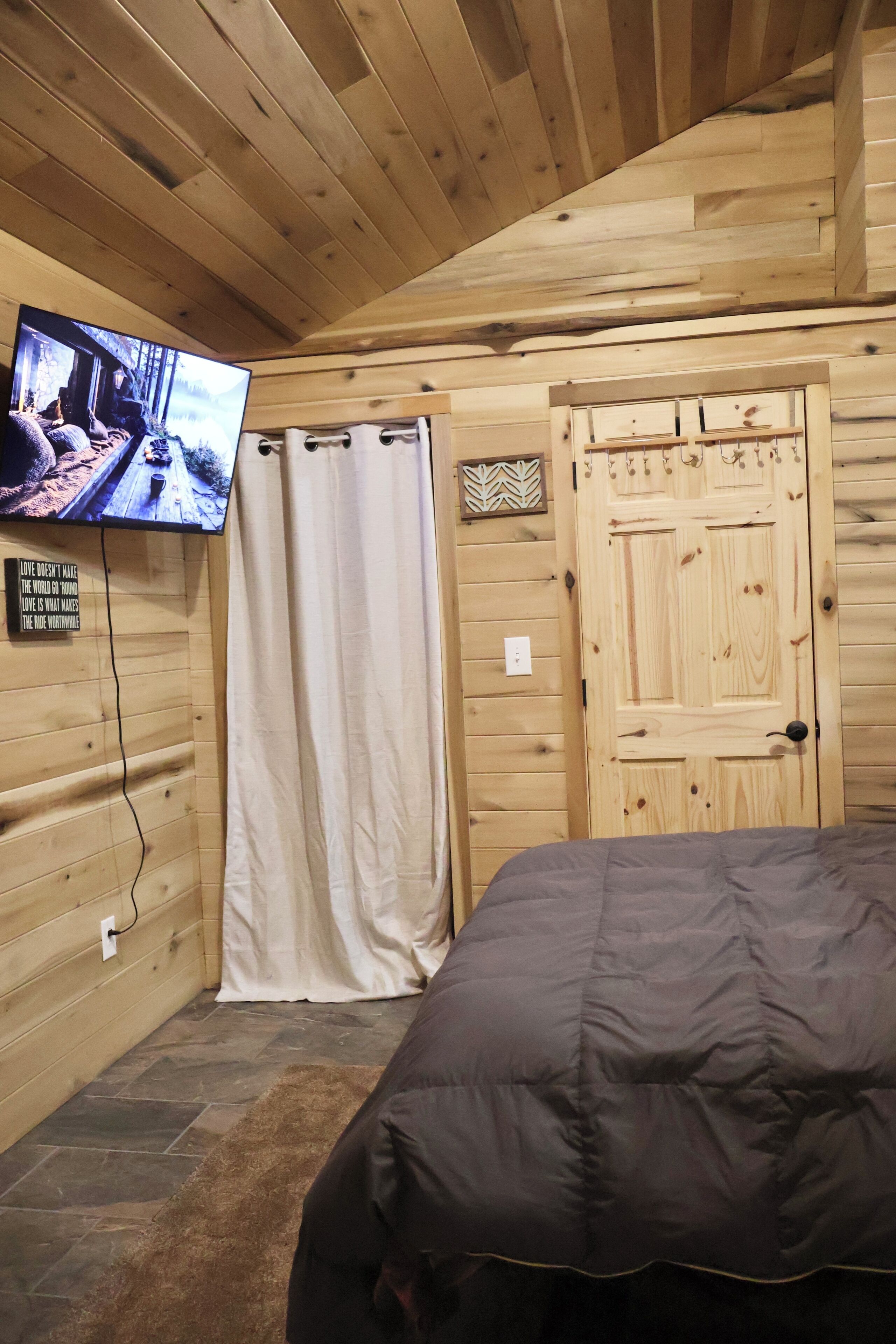 Una habitación de cabaña de madera con una cama, un televisor, una puerta de madera y suelo de piedra.
