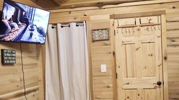 Una habitación de cabaña de madera con una cama, un televisor, una puerta de madera y suelo de piedra.