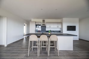 A modern kitchen with a central island, bar stools, and a flat-screen TV.