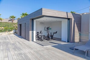 Un gimnasio moderno al aire libre con equipo de ejercicio, una terraza de madera y cielo despejado.