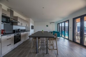 A modern kitchen with a dining area, large windows, and a view of the outdoors. - Lecci Villa With Outdoor Pools (Lecci)