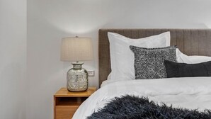 Een net opgemaakt bed met patroon kussens, een bedlamp en een klein houten nachtkastje.