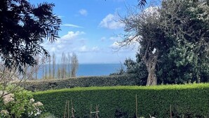 A garden with a large rock, neatly trimmed hedges, and a view of the sea. - Rental for 2 With Private Outdoor Space (Plougasnou)