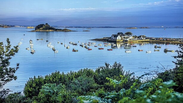A coastal scene with boats, a small island, and a building with a white facade. - Rental for 2 With Private Outdoor Space (Plougasnou)