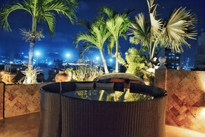 Eine Dachterrasse mit Whirlpool, Palmen und Blick auf die nächtliche Stadtlandschaft.