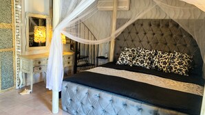 Ein Schlafzimmer mit einer geblümten Kopfteile, einem Bett mit schwarz-weißen Kissen, einem Nachttisch, einem Spiegel und einer Nachttischlampe.