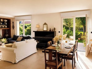Ein Wohnzimmer mit einer Couch, einem Esstisch mit Stühlen, einem Klavier und einem Fernseher.