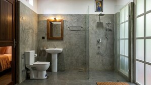 Een moderne badkamer met douche, toilet en wastafel, met een houten plafond en grote ramen.