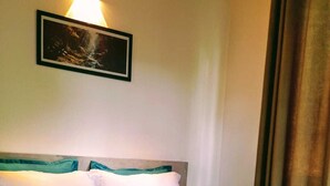 Een hotelkamer met een bed, kussens, een ingelijst schilderij aan de muur en een raam met gordijnen.