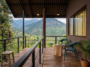 A wooden deck with a railing, a table, chairs, and a potted plant.
