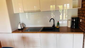 A compact kitchen with a sink, a kettle, a coffee maker, and a bottle of dish soap.