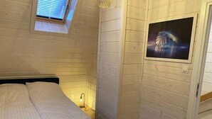 Et soveværelse med en seng, et lille vindue, et billede hængt på væggen og en lampe på sengebordet.