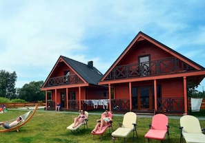 A red wooden building with a balcony and a grassy area with lounge chairs. - Air-conditioned Holiday Homes With Swimming Pool (Mielno)