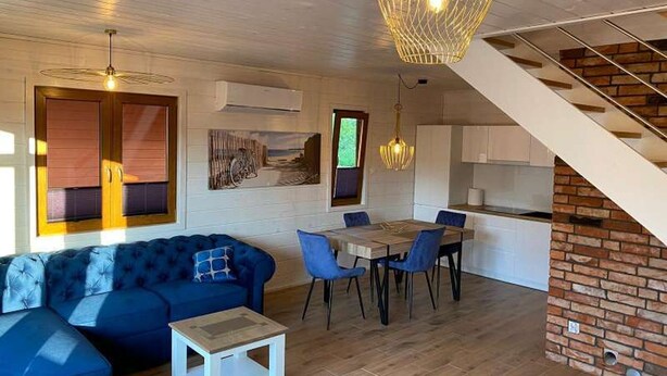 Et moderne interiør med en blå sofa, spisebord, stole, en trappe og en hængende lampe.