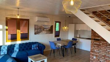 Un interior moderno con un sofá azul, una mesa de comedor y sillas, una escalera y una lámpara colgante.