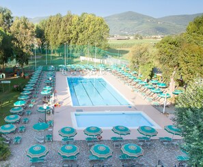 Ein Pool umgeben von Liegestühlen und Sonnenschirmen, mit Blick auf Bäume und Hügel im Hintergrund.
