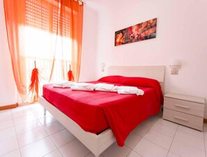 A bedroom with a bed, curtains, a painting, and a nightstand. - 4-person Coastal Apartment Near Tuscany (Luni)