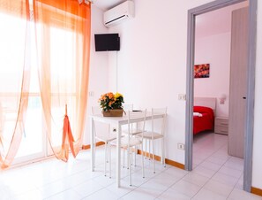 A hotel room with a dining area, a TV mounted on the wall, and a red bed. - 4-person Coastal Apartment Near Tuscany (Luni)