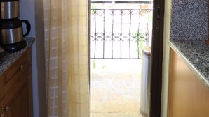 A kitchen with wooden cabinets, a countertop, and a window with a curtain. - Charming Glyfada Family Appartment close to the Beach & City center | Quiet Area (Glifada)