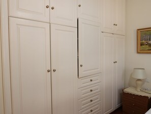 Une pièce avec des armoires blanches, une commode, une lampe et un tableau au mur.
