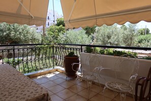 Un balcon avec une table et des chaises, un pot de fleurs et une vue sur les arbres et les bâtiments.