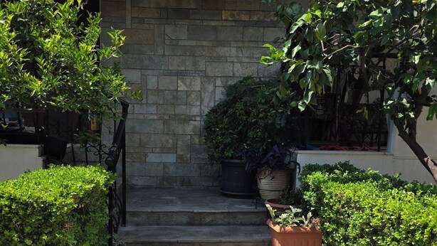 A stone pathway leading to a building entrance with steps, potted plants, and a small garden area. - Charming Glyfada Family Appartment close to the Beach & City center | Quiet Area (Glifada)